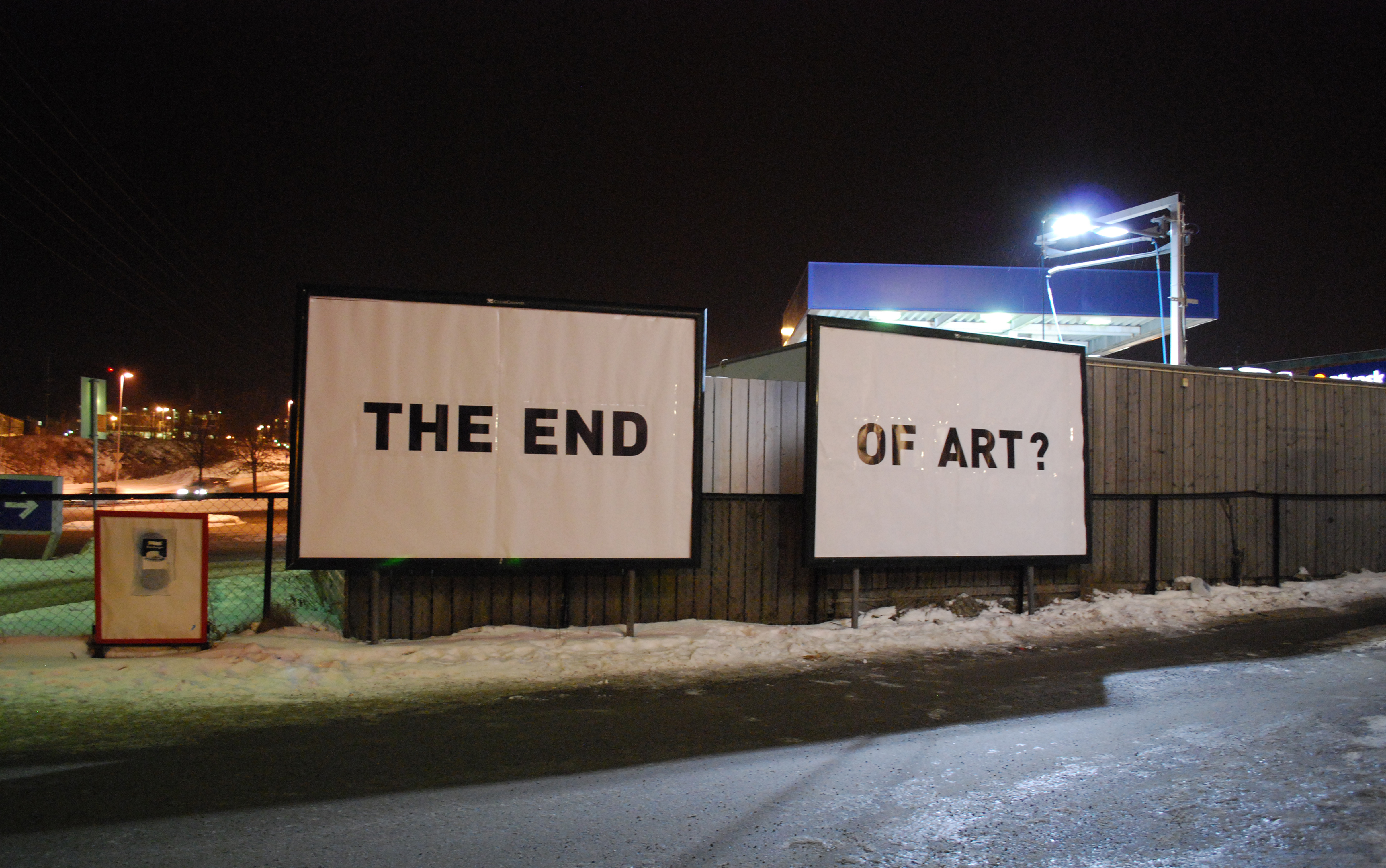 Two illuminated billboards reading 'THE END OF ART?' at night in a snowy industrial landscape